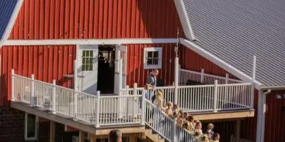 A bride and groom walking on a lawn toward a large red barn with white trim and a metal roof.