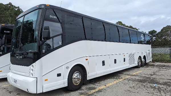 A white charter bus parked in a lot with a second bus partially visible in the background.
