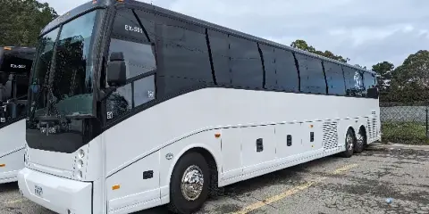 A white charter bus parked in a lot with a second bus partially visible in the background.