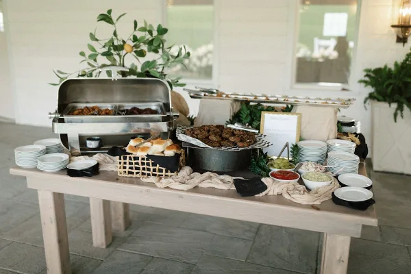 A catering buffet table featuring chafing dishes, a basket of rolls, and various food items.