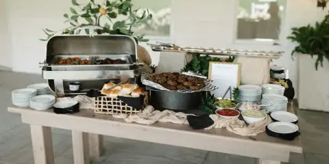 A catering buffet table featuring chafing dishes, a basket of rolls, and various food items.