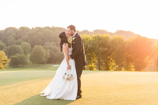 A bride and groom kissing on a golf course during golden hour.