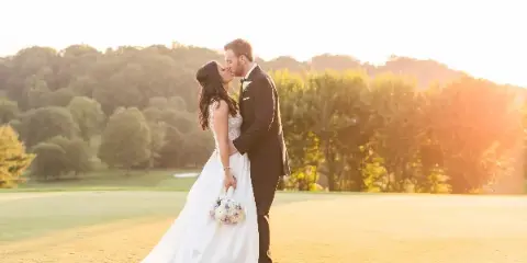 A bride and groom kissing on a golf course during golden hour.