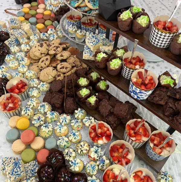 A catering table filled with an assortment of desserts including macarons, chocolate brownies, cookies, and cups of fresh strawberries.