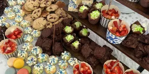 A catering table filled with an assortment of desserts including macarons, chocolate brownies, cookies, and cups of fresh strawberries.