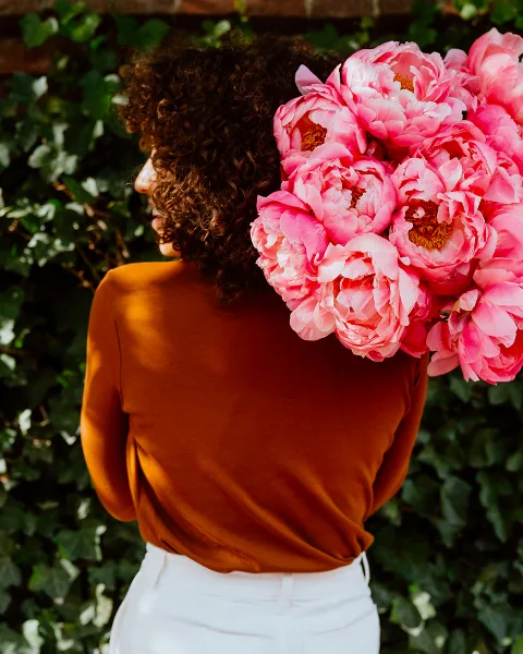 A person holding a large bouquet of pink peonies against a background of green ivy.