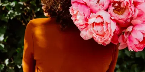 A person holding a large bouquet of pink peonies against a background of green ivy.
