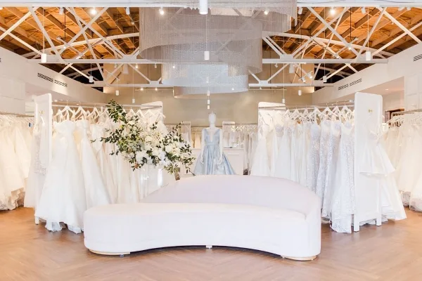 Interior of a bridal boutique with rows of white wedding dresses and a central seating area.