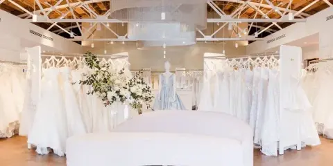 Interior of a bridal boutique with rows of white wedding dresses and a central seating area.