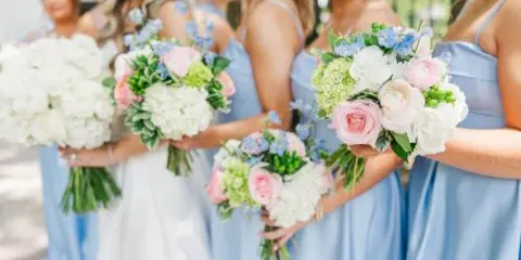 A bride and bridesmaids in blue dresses holding white, pink, and blue wedding bouquets.