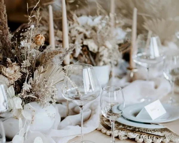 A close-up of an elegant wedding table setting featuring dried floral arrangements, tall candles, and glassware.
