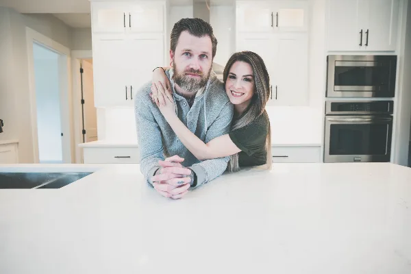 A professional portrait of a smiling couple posing together in a modern kitchen.
