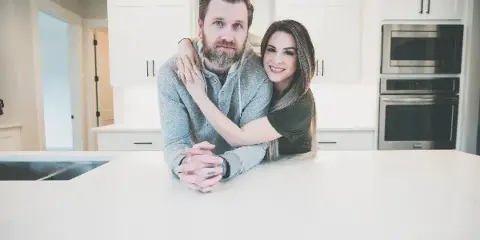 A professional portrait of a smiling couple posing together in a modern kitchen.