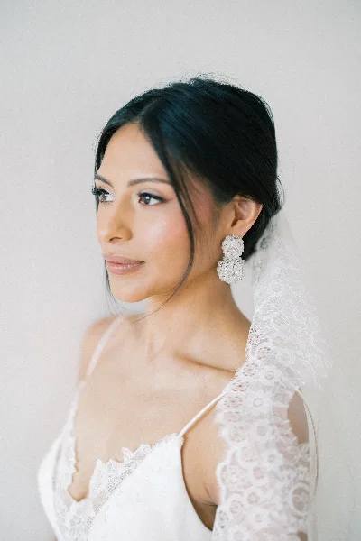 A bride in a white lace dress and veil with professional makeup and hair styling.
