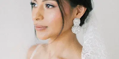 A bride in a white lace dress and veil with professional makeup and hair styling.