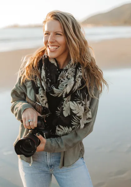 A smiling woman holding a professional camera on a beach