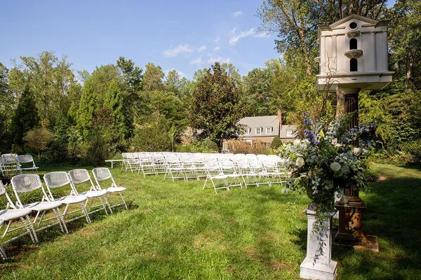 Outdoor wedding ceremony setup with white chairs and floral arrangements on a grassy lawn.