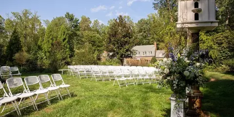 Outdoor wedding ceremony setup with white chairs and floral arrangements on a grassy lawn.