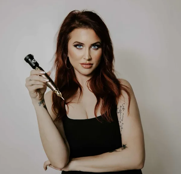 A professional portrait of a woman with red hair and full makeup holding a makeup brush.