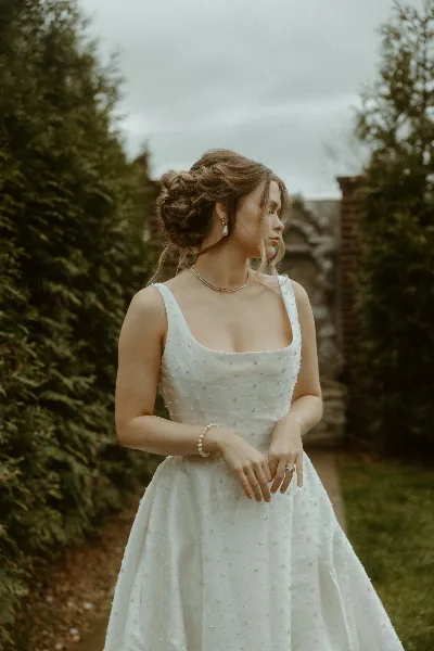 A bride in a white wedding dress standing outdoors in a garden setting.