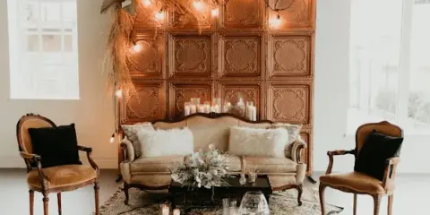 A styled event lounge featuring a vintage sofa, two accent chairs, a patterned rug, and a decorative backdrop with string lights.