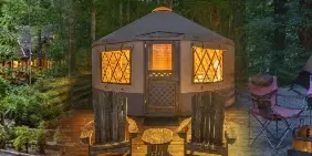 A park lodge, a yurt, and a group shelter in a wooded area with people sitting outside.
