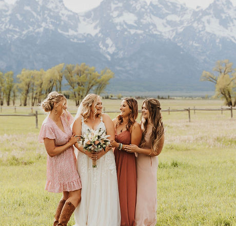 A bride and three bridesmaids standing together in a grassy field with mountains in the background.