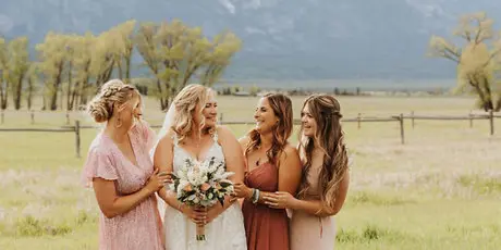A bride and three bridesmaids standing together in a grassy field with mountains in the background.