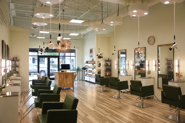 Interior view of a modern hair salon featuring green styling chairs, mirrors, and product shelves.