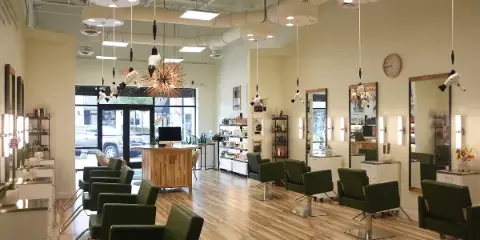 Interior view of a modern hair salon featuring green styling chairs, mirrors, and product shelves.