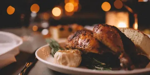 A close-up of a plated roasted chicken dish with garlic and herbs on a table with warm bokeh lighting.