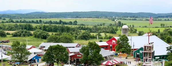 Aerial view of a rural fairground featuring red barns, a silo, and green fields.