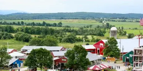 Aerial view of a rural fairground featuring red barns, a silo, and green fields.