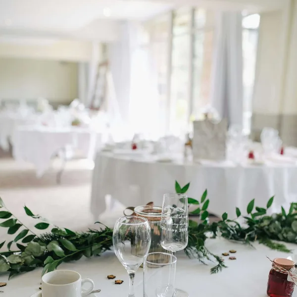 A close-up of a wedding table setting with white linens, glassware, and a greenery runner.