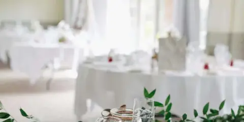 A close-up of a wedding table setting with white linens, glassware, and a greenery runner.