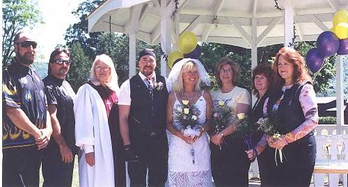 A wedding party, including the bride, groom, and officiant, posing together outdoors after a ceremony.
