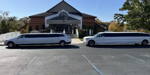 Two white stretch limousines parked in a lot in front of a brick church building.