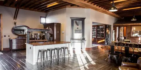 Interior of a historic wooden event venue with exposed beams, a bar, stools, and seating area