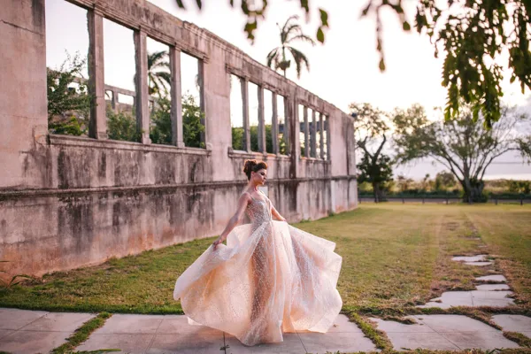 A bride in a flowing white wedding dress posing outdoors near a historic stone structure.