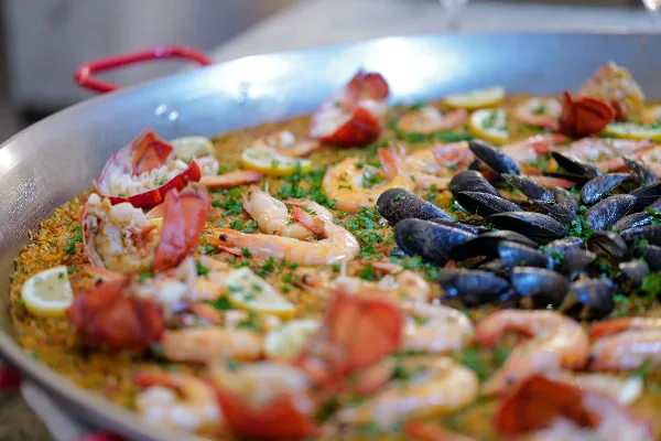 A large pan of seafood paella featuring shrimp, mussels, and lobster tails garnished with herbs and lemon slices.