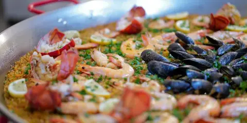 A large pan of seafood paella featuring shrimp, mussels, and lobster tails garnished with herbs and lemon slices.