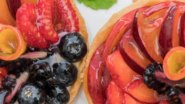 Close-up of two fresh fruit tarts topped with raspberries, blueberries, and glazed peaches.