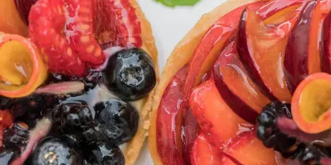 Close-up of two fresh fruit tarts topped with raspberries, blueberries, and glazed peaches.