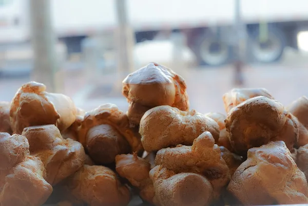 A pile of golden-brown, puffy popovers stacked together in a bakery setting.
