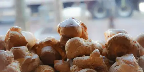 A pile of golden-brown, puffy popovers stacked together in a bakery setting.