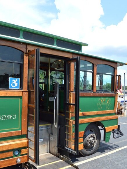 Exterior view of a green and wood-paneled trolley with open doors and a wheelchair accessibility sticker.