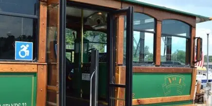 Exterior view of a green and wood-paneled trolley with open doors and a wheelchair accessibility sticker.