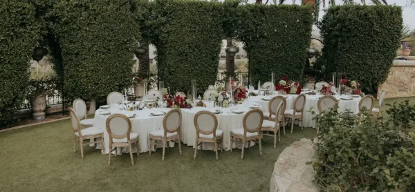 A round event table set with white tablecloth, chairs, and floral centerpieces in an outdoor venue.