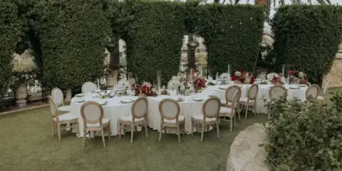 A round event table set with white tablecloth, chairs, and floral centerpieces in an outdoor venue.