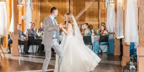 A bride and groom dancing at a wedding reception inside a rustic wooden barn venue.